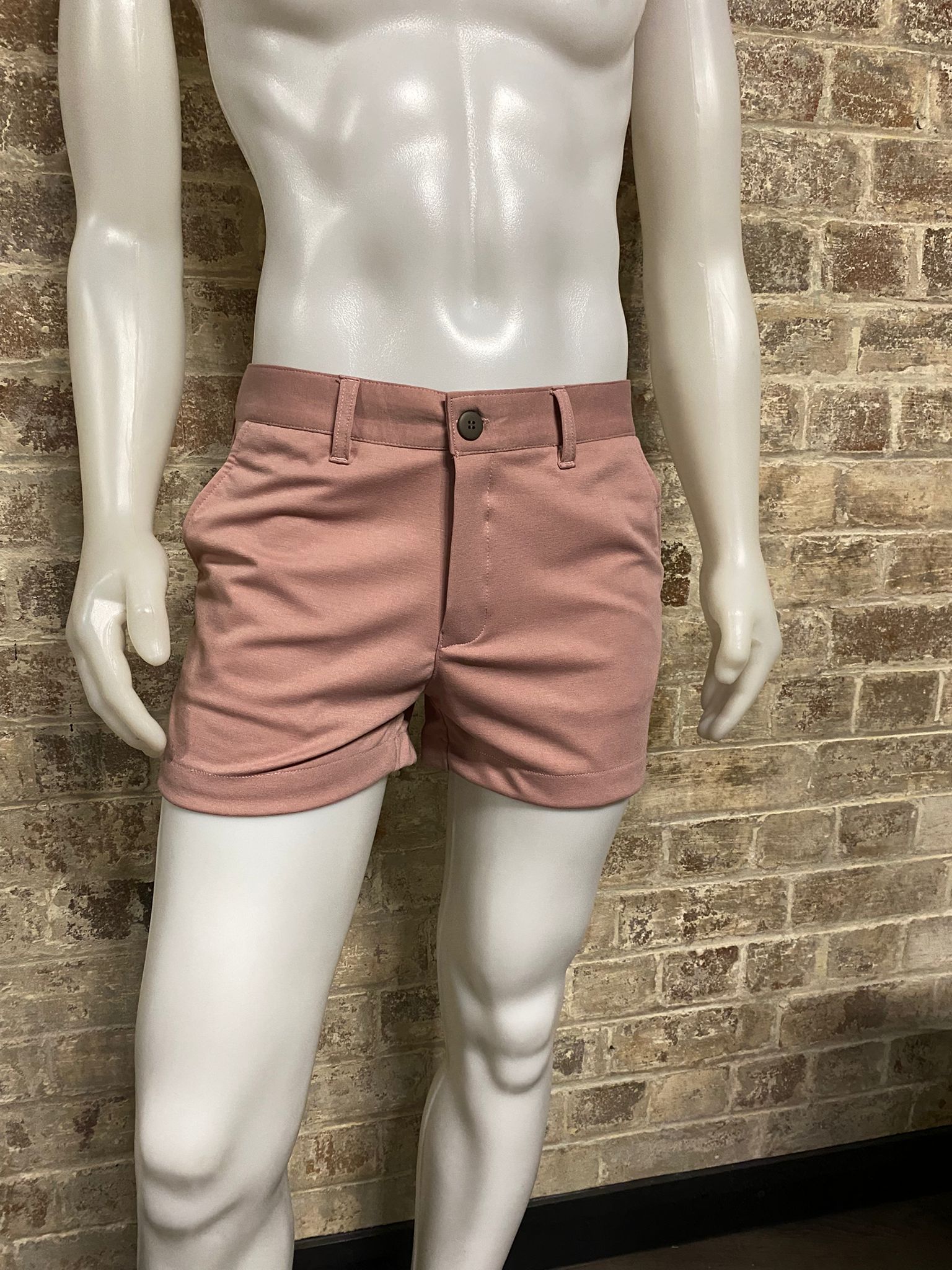 Mannequin wearing pink shorts against a brick wall