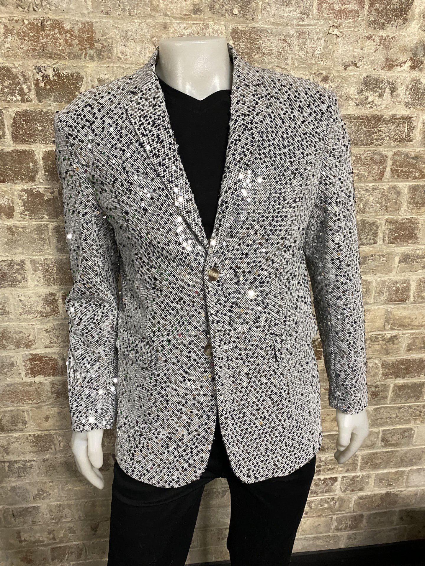 Silver sequin blazer on a mannequin against a brick wall.